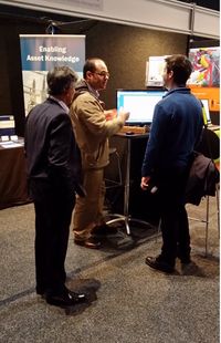 A man stands infront of a conference booth demonstrating on a computer screen to a delegate